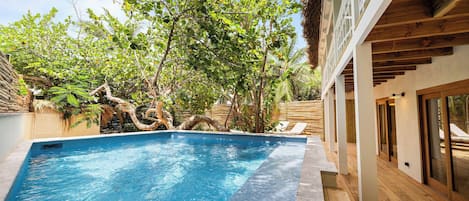 A swimming pool with wooden deck and lounge chairs, surrounded by lush greenery and trees.