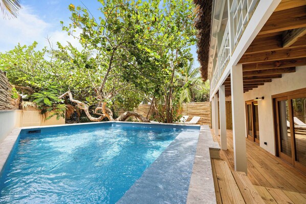 A swimming pool with wooden deck and lounge chairs, surrounded by lush greenery and trees. - Sorobon Luxury Beach Resort (Kralendijk)