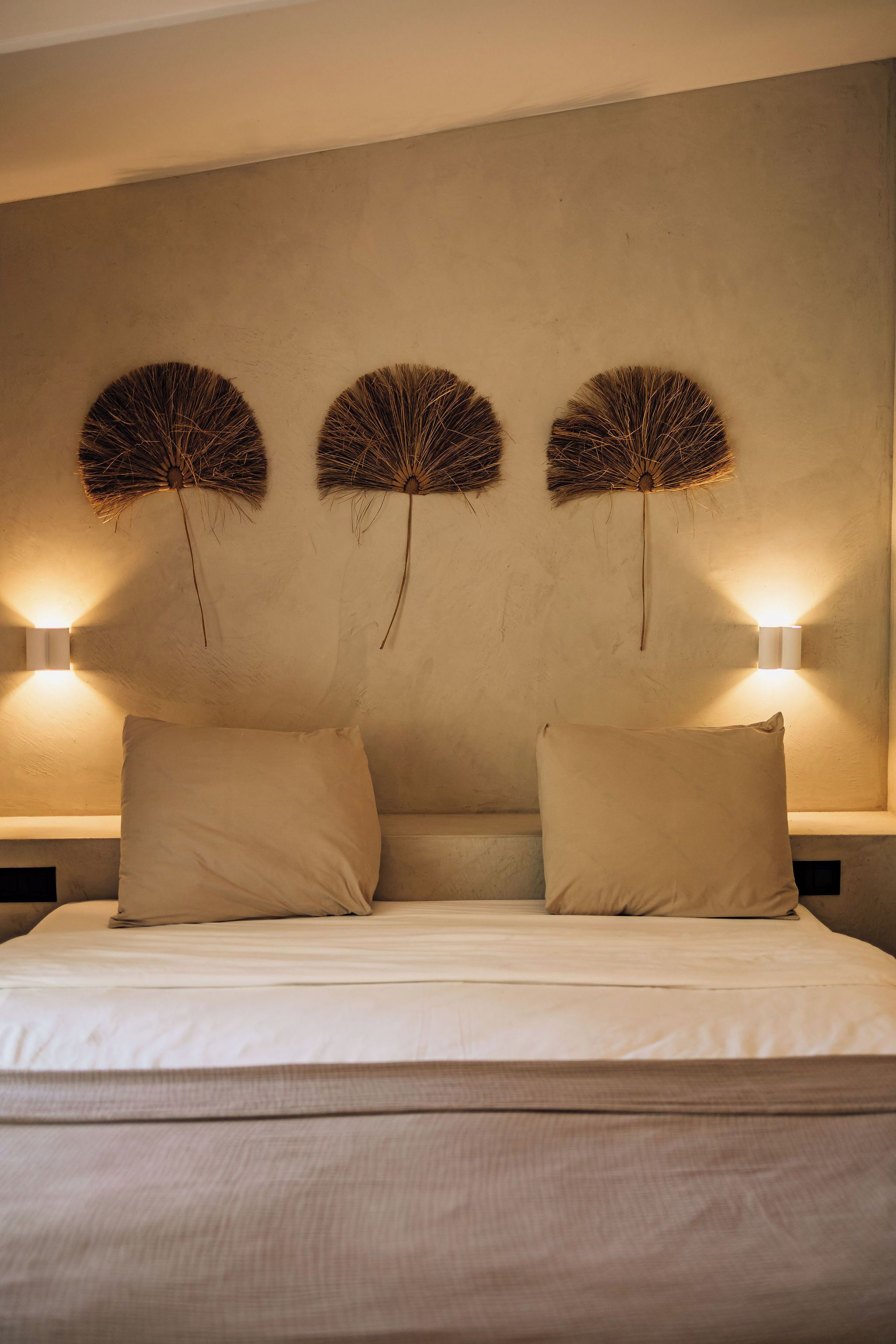 A bed with two pillows and three wall-mounted light fixtures.