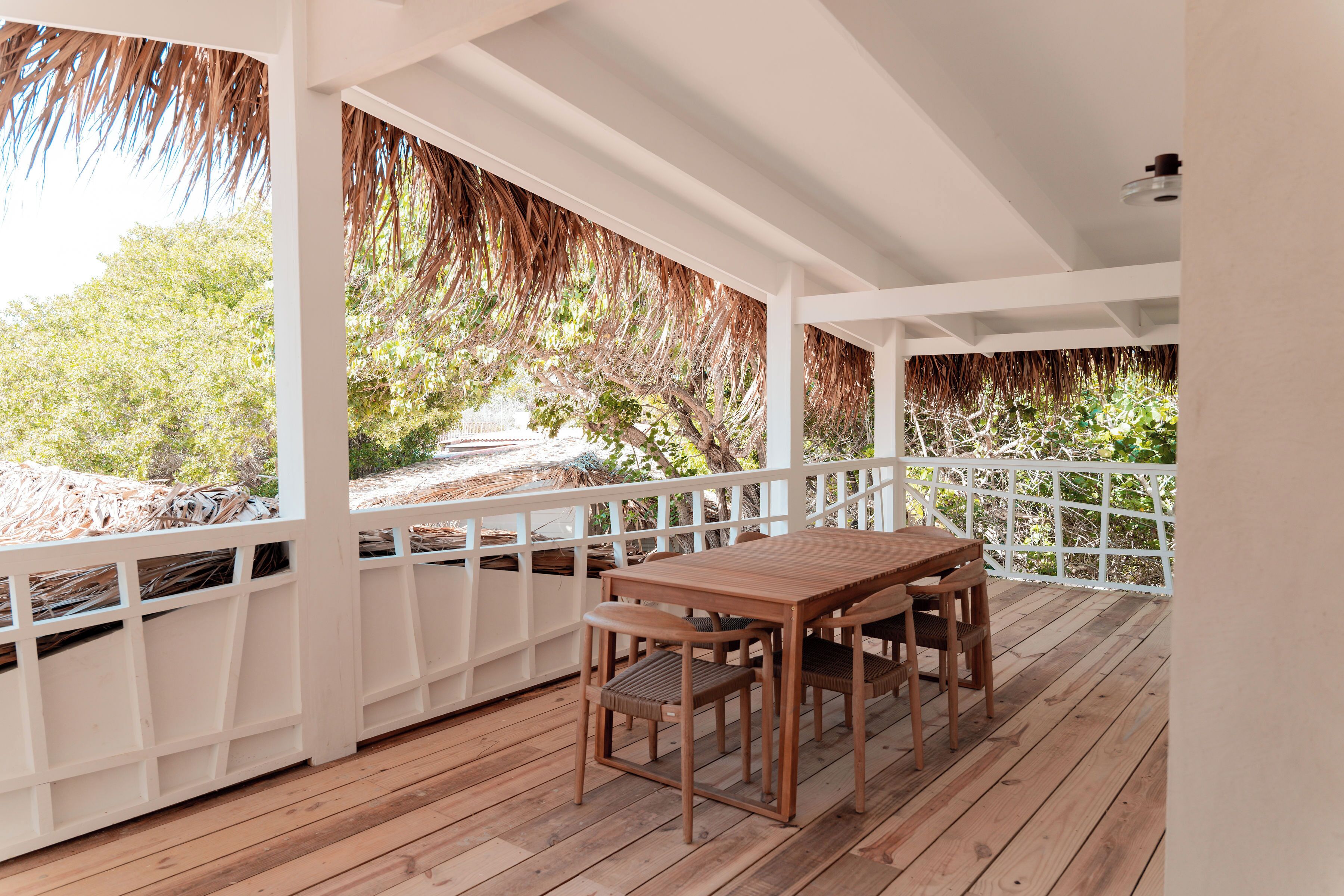 A wooden deck with a table and chairs, surrounded by white railings and lush greenery.