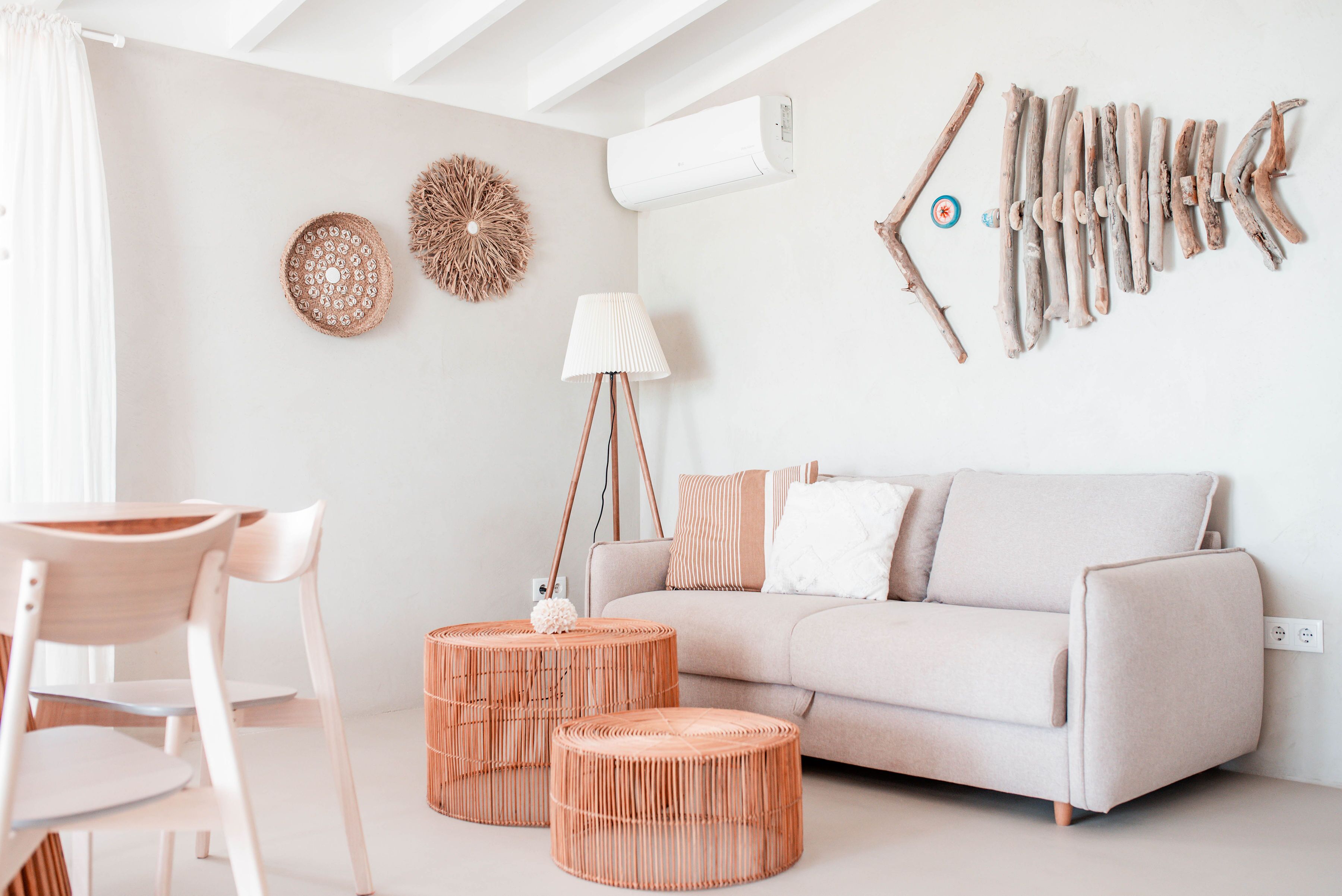 Un salon moderne comprenant un canapé, deux poufs ronds en osier, une lampe sur pied et des éléments de décoration murale.