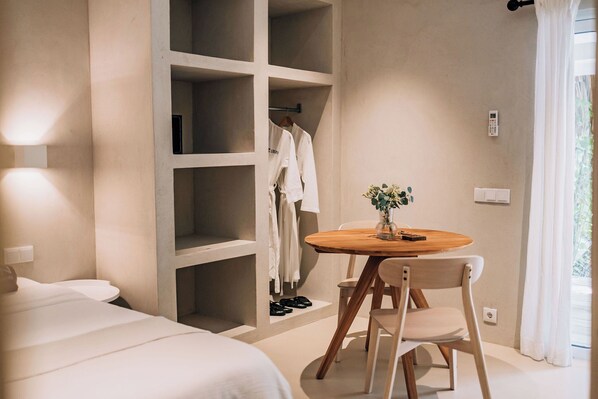 Un dormitorio con una cama, una mesa de madera con sillas, un armario y una planta pequeña.