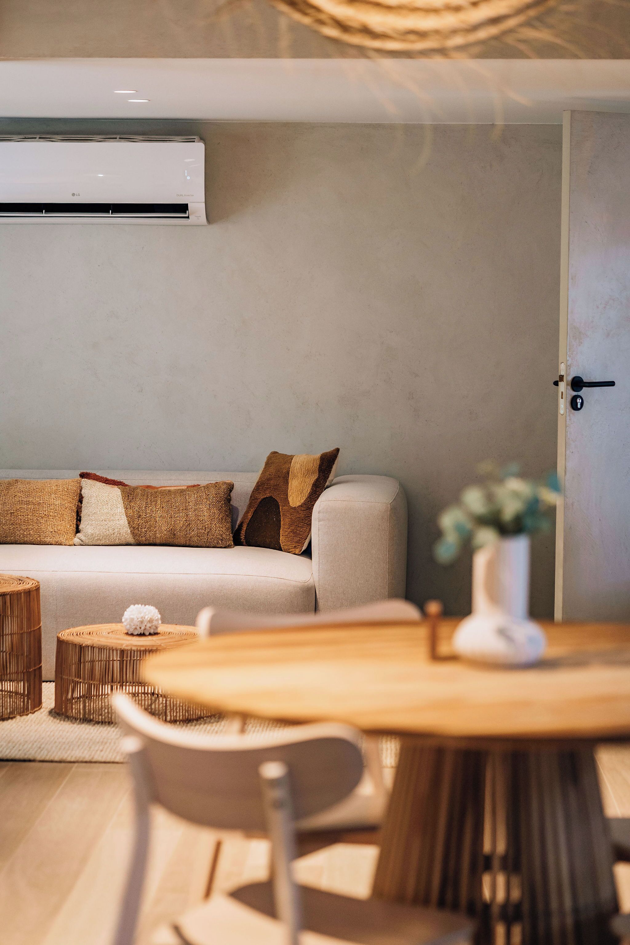 A modern living room with a sofa, a dining table, and a wall-mounted air conditioner.
