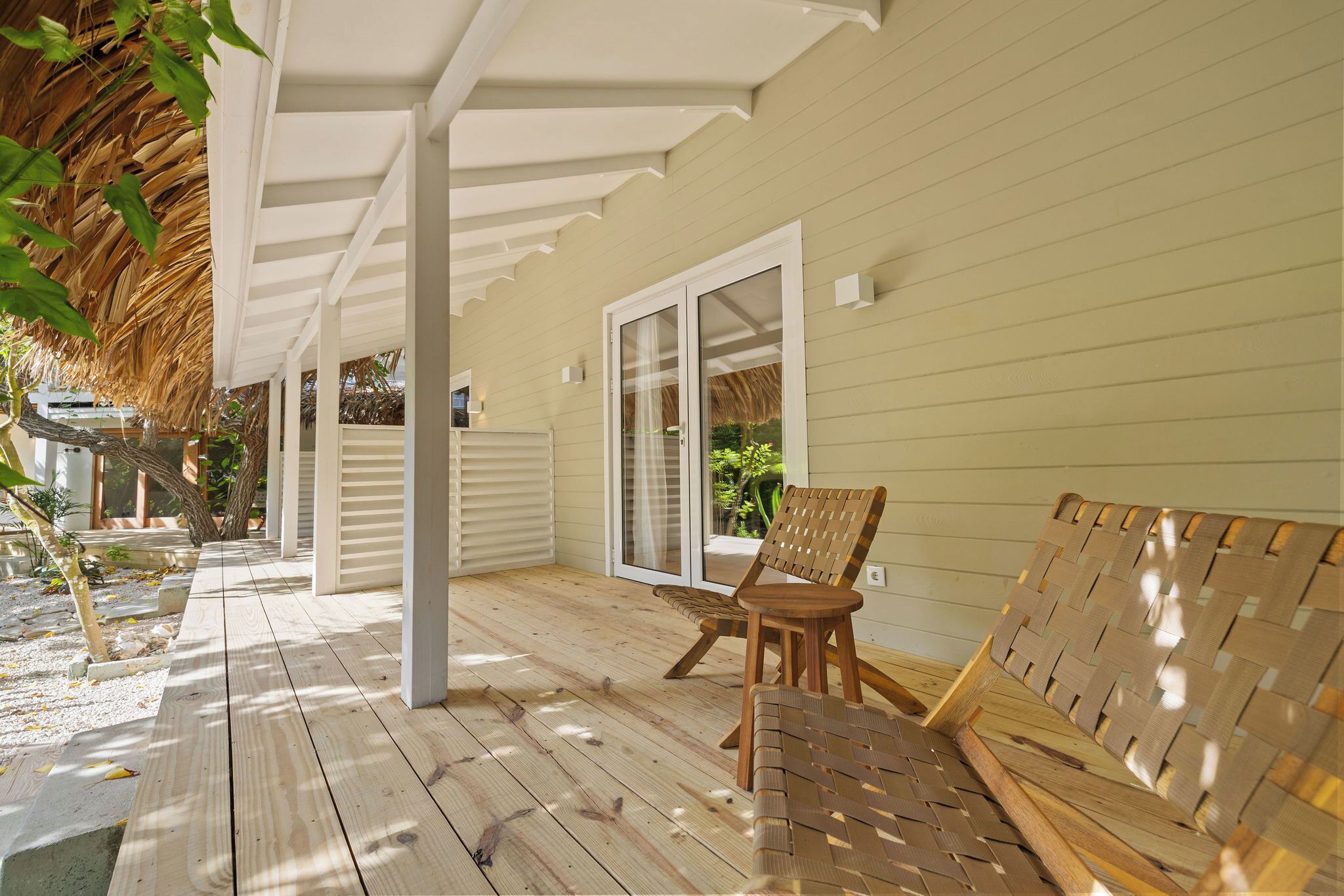 A covered wooden deck with a bench and a woven chair, leading to a sliding glass door.
