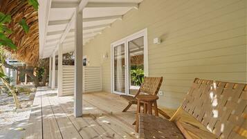 A covered wooden deck with a bench and a woven chair, leading to a sliding glass door.