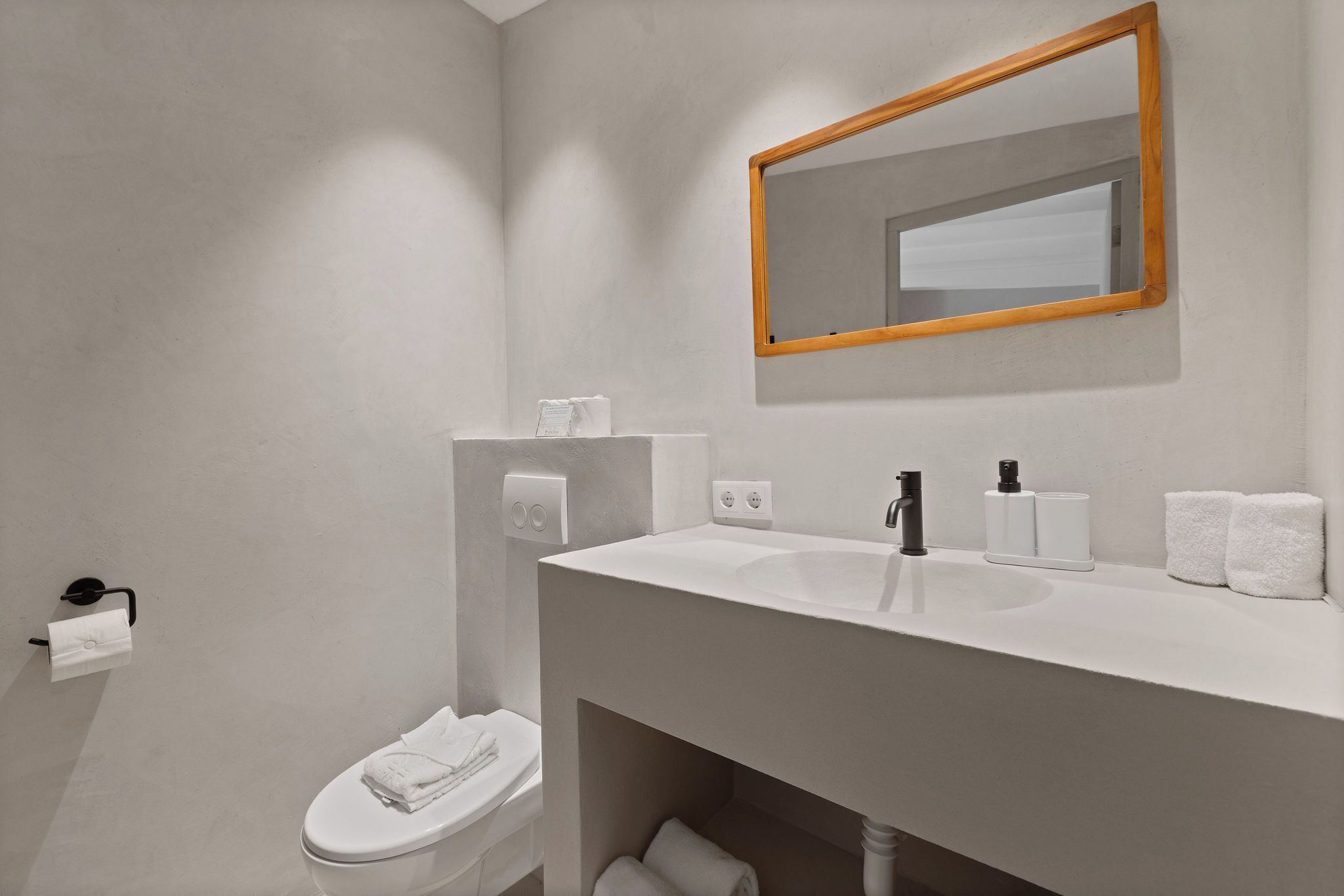 Un baño moderno con lavamanos, espejo y retrete blancos.