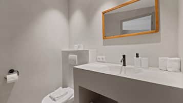 Un baño moderno con lavamanos, espejo y retrete blancos.
