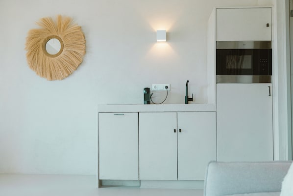 A kitchen with white cabinets, a microwave, a coffee maker, and a wall-mounted light fixture. - Sorobon Luxury Beach Resort (Kralendijk)