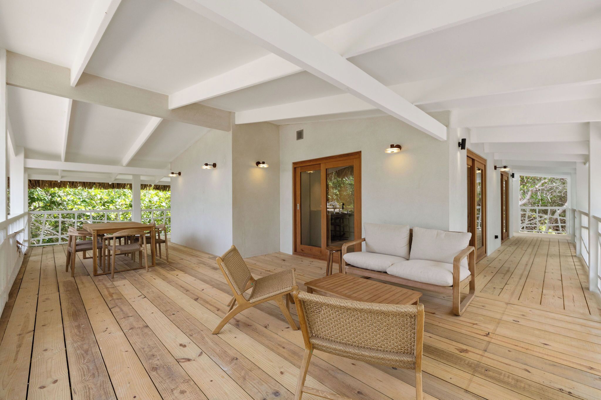 Una terraza de madera con una mesa, sillas, un sofá y un ventanal corredero que da a un balcón.