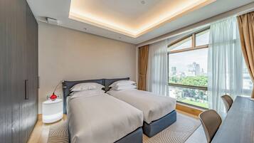 A modern hotel room with two beds, a dining table, and a large window with a city view.