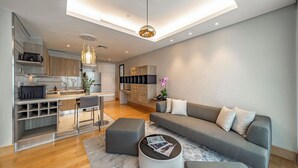 Een moderne woonkamer met een grijze bank, een salontafel, en een keuken in de achtergrond.