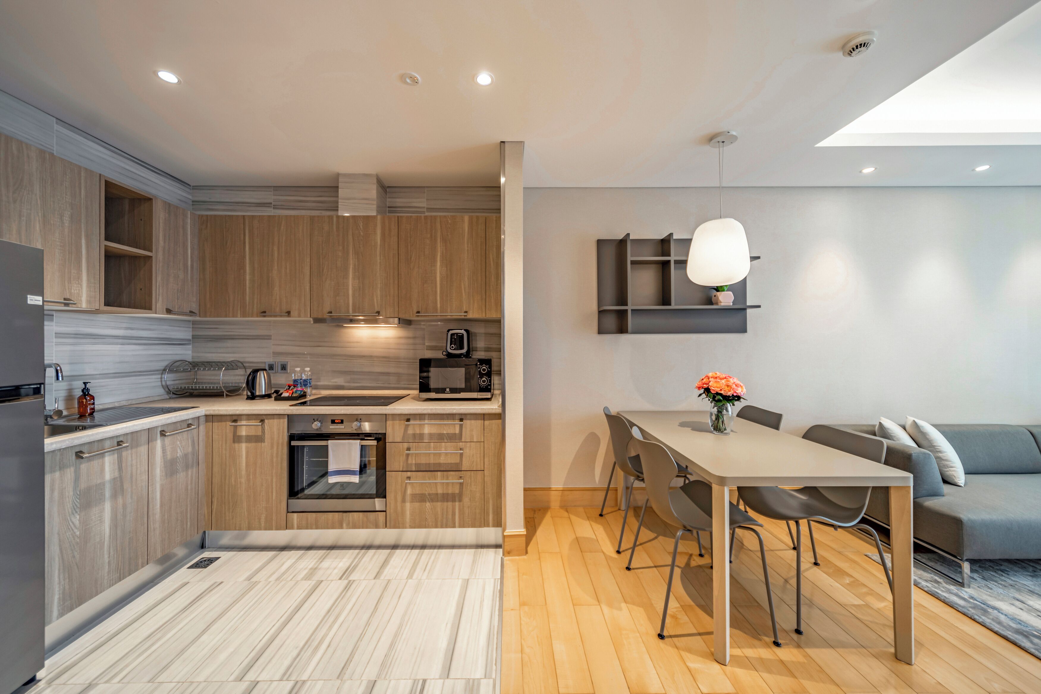 A modern kitchen with wooden cabinets, a dining area with a table and chairs, and a built-in oven.