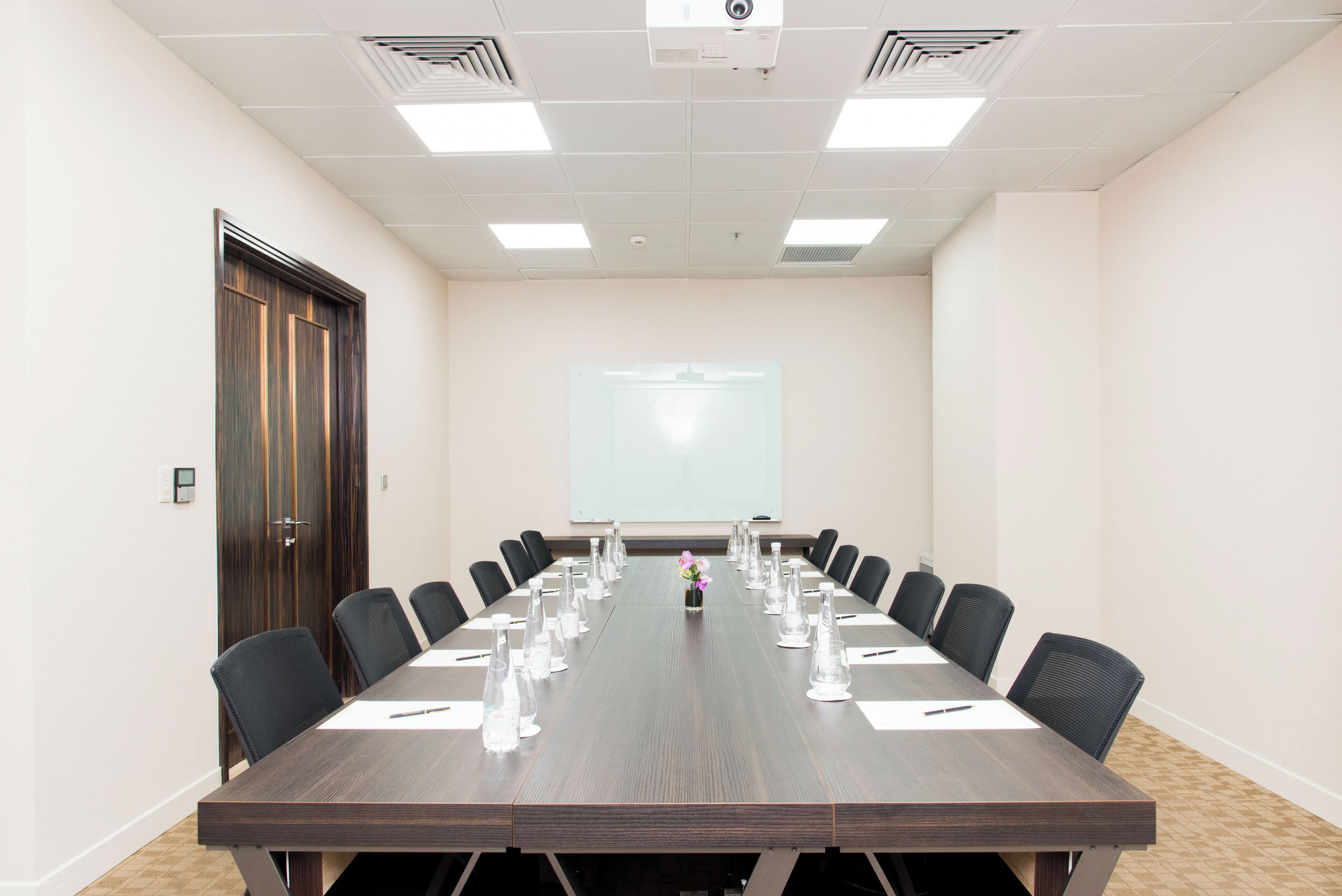Ein Konferenzraum mit einem langen Tisch, Stühlen, einer Projektionsleinwand und einer Tür.