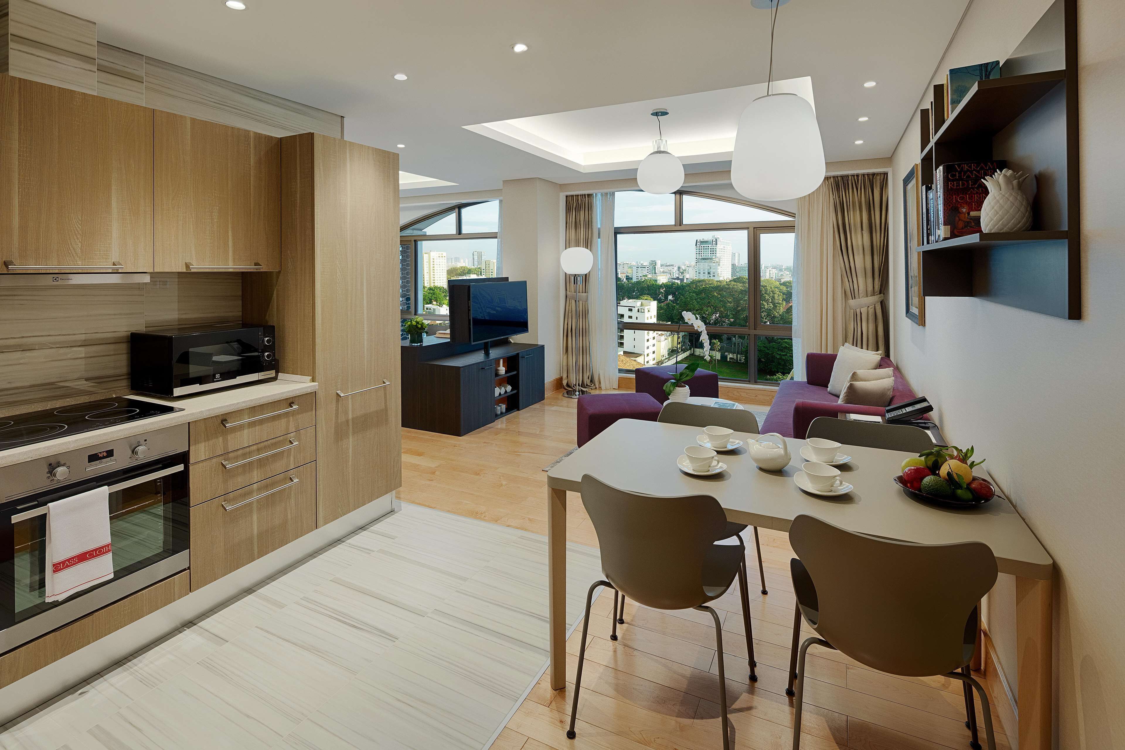A modern kitchen with wooden cabinets, a dining area with a table and chairs, and a living area with a sofa and a TV.