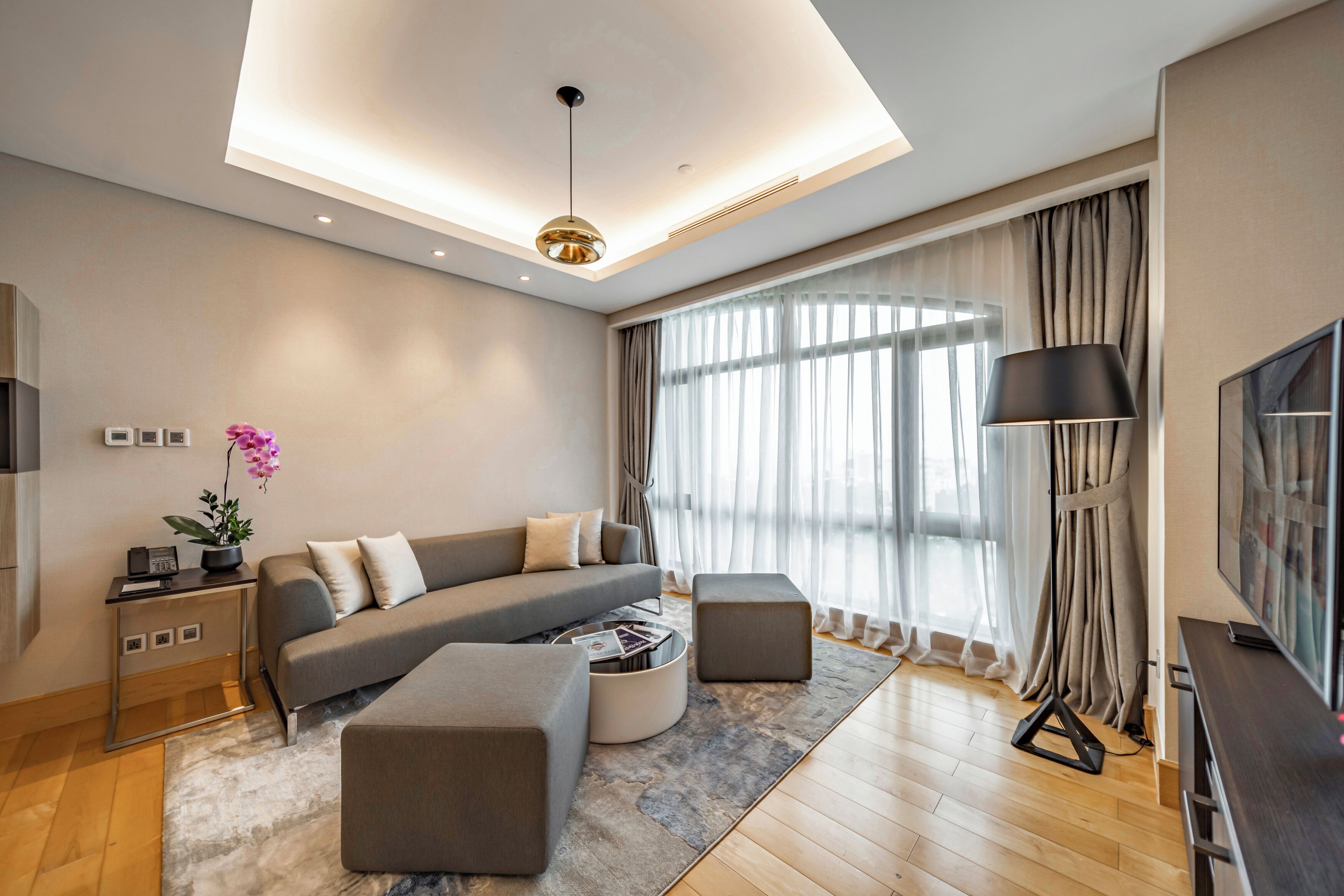 Un salon moderne avec un canapé, des poufs, une table basse, un téléviseur et une lampe.
