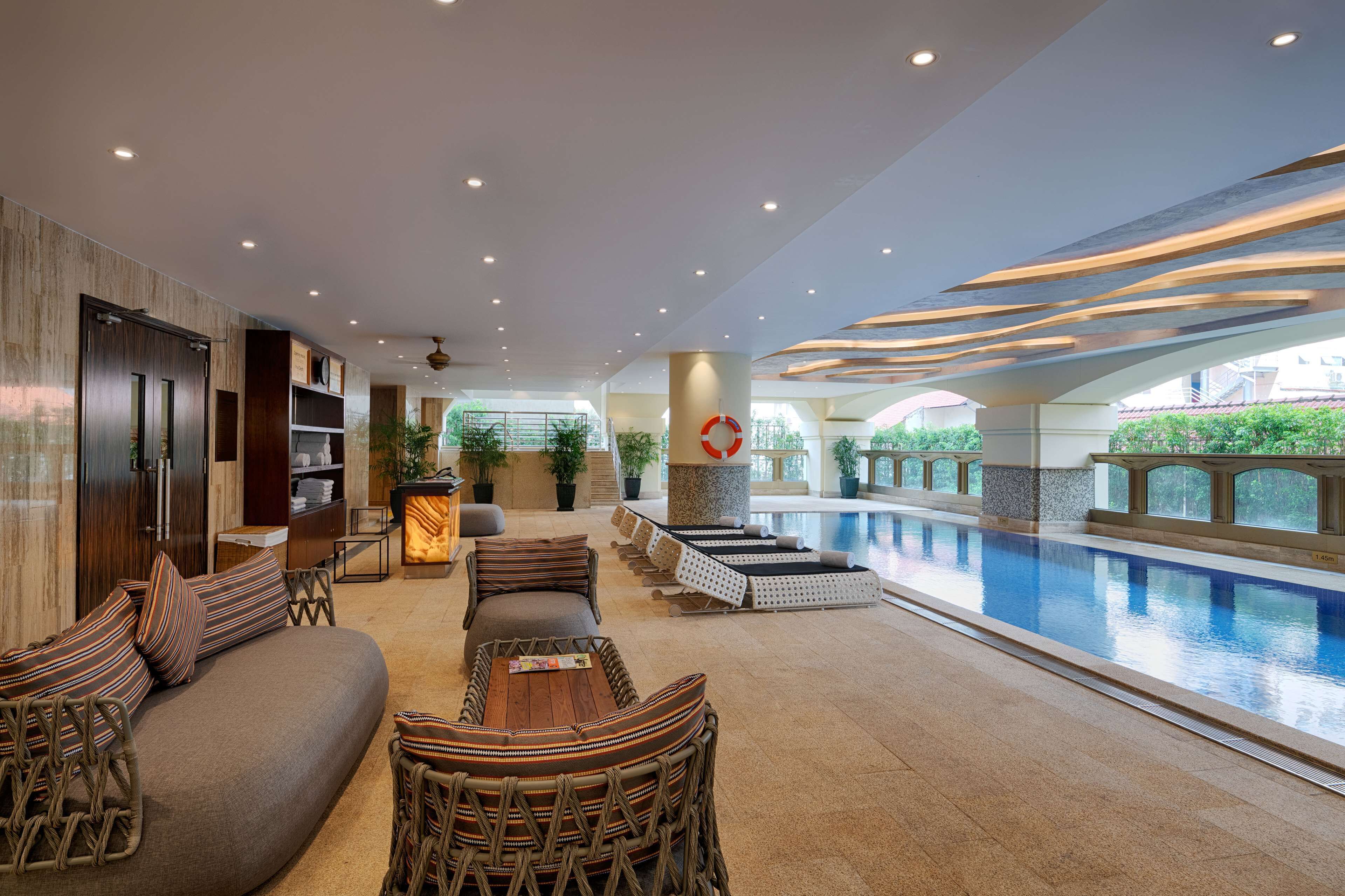 Un espace piscine intérieur moderne, doté d’un coin salon, d’un comptoir d’accueil et offrant une vue sur la piscine.