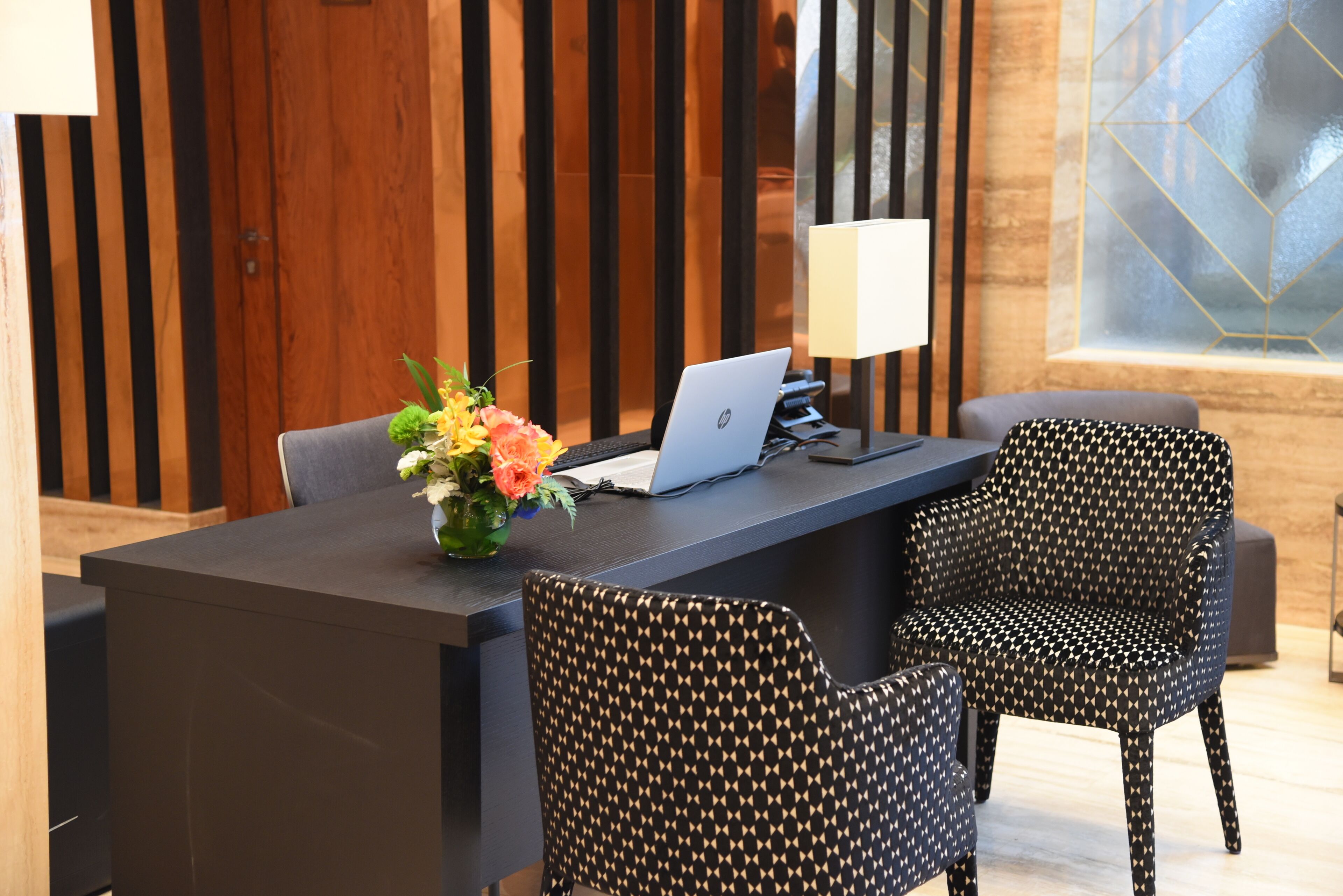Un mostrador de recepción moderno con una computadora portátil, un florero y sillas con estampado.