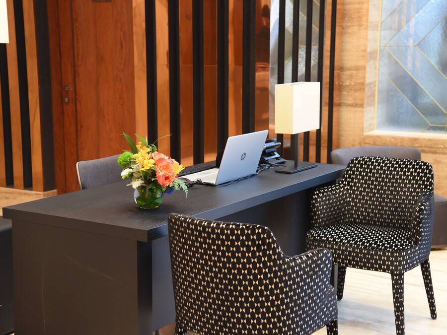 Un mostrador de recepción moderno con una computadora portátil, un florero y sillas con estampado.