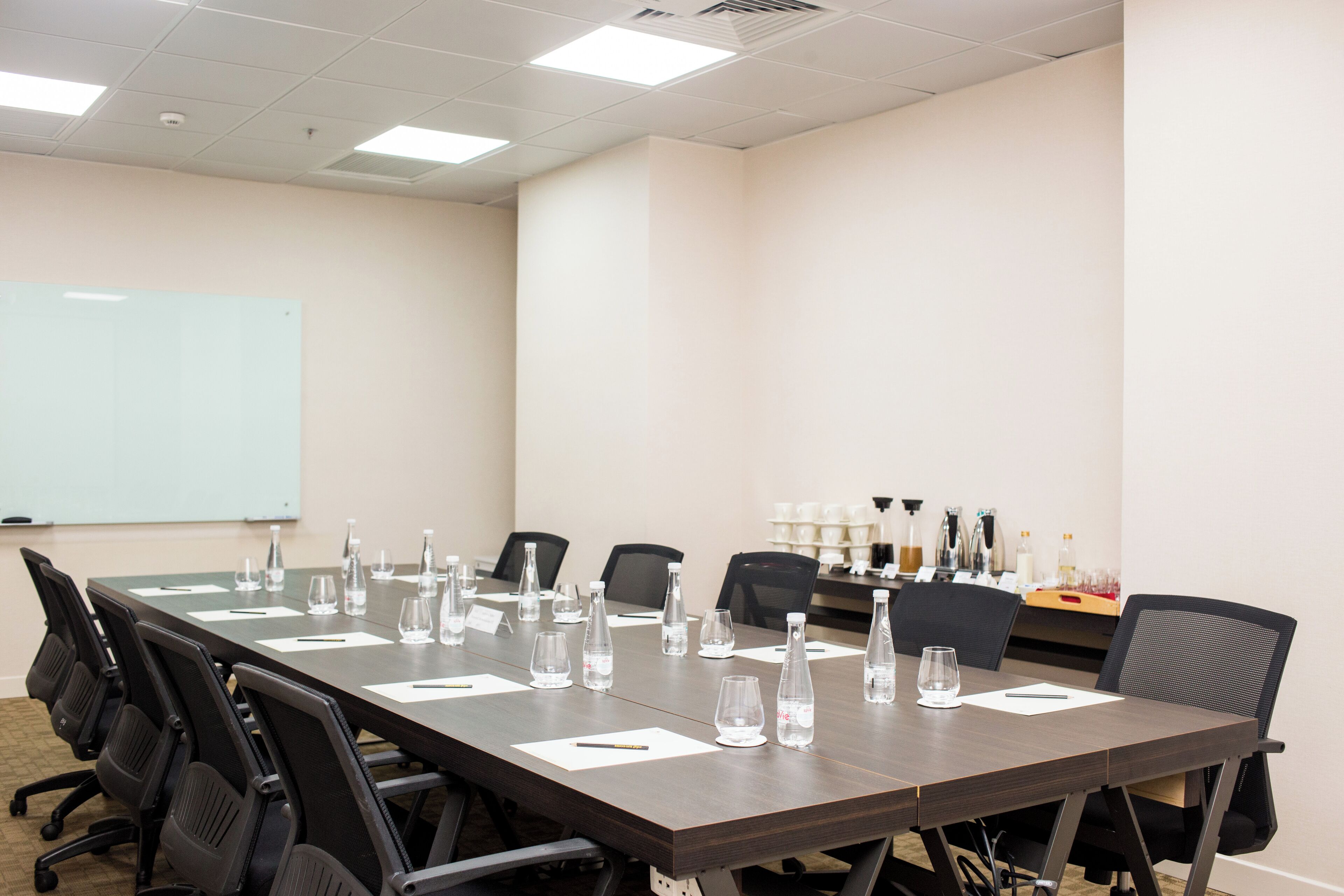 Un salón de conferencias con una larga mesa, sillas, botellas de agua y una pizarra.