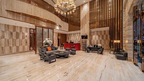 A spacious lobby with a high ceiling, a central chandelier, a reception desk, and a seating area with sofas and chairs.