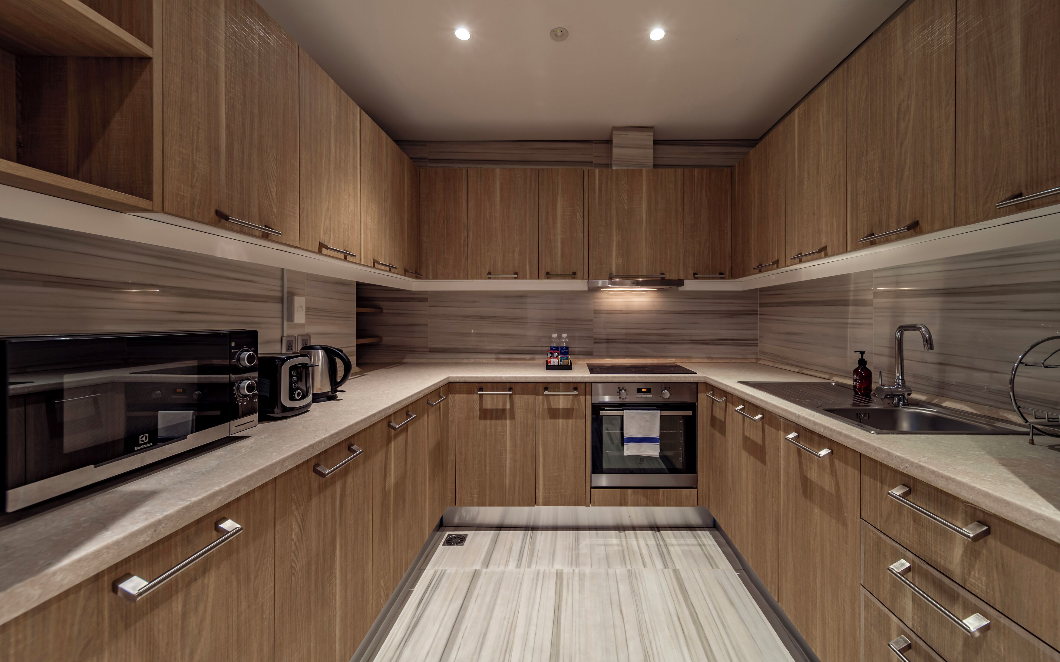 A modern kitchen with wooden cabinets, a built-in oven, a microwave, and a coffee maker.
