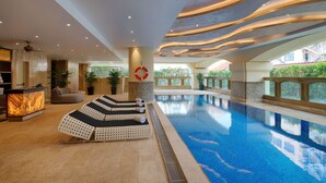 Een modern binnenzwembad met lounge fauteuils, een receptie en uitzicht op de omgeving.