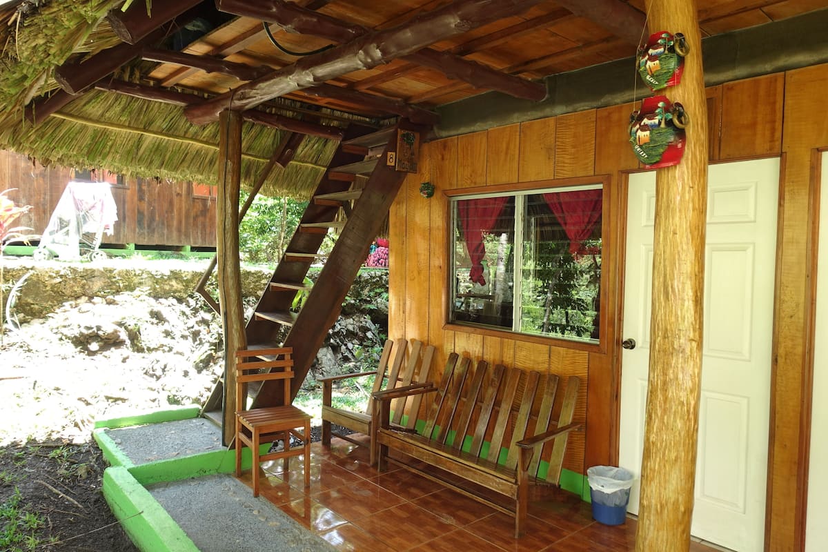 Una cabaña de madera con techo de paja, una escalera de madera, un banco y una ventana con vistas al exterior.