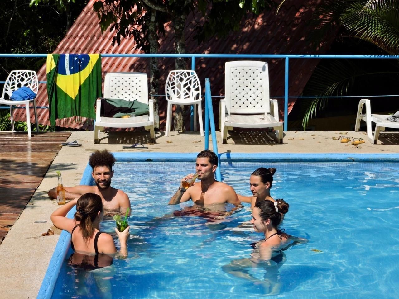 A swimming pool with people enjoying the water, surrounded by white chairs and a Brazilian flag.