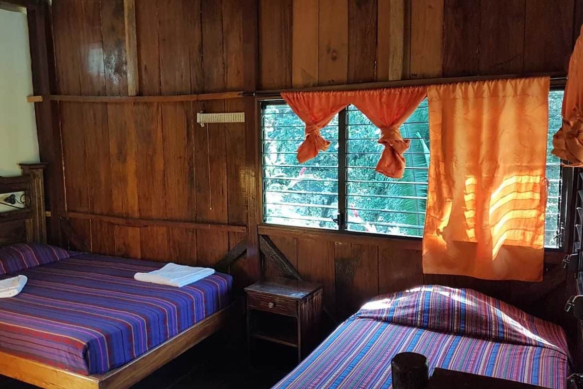 Una habitación de cabaña de madera con dos camas, una mesita pequeña y una ventana con cortinas.
