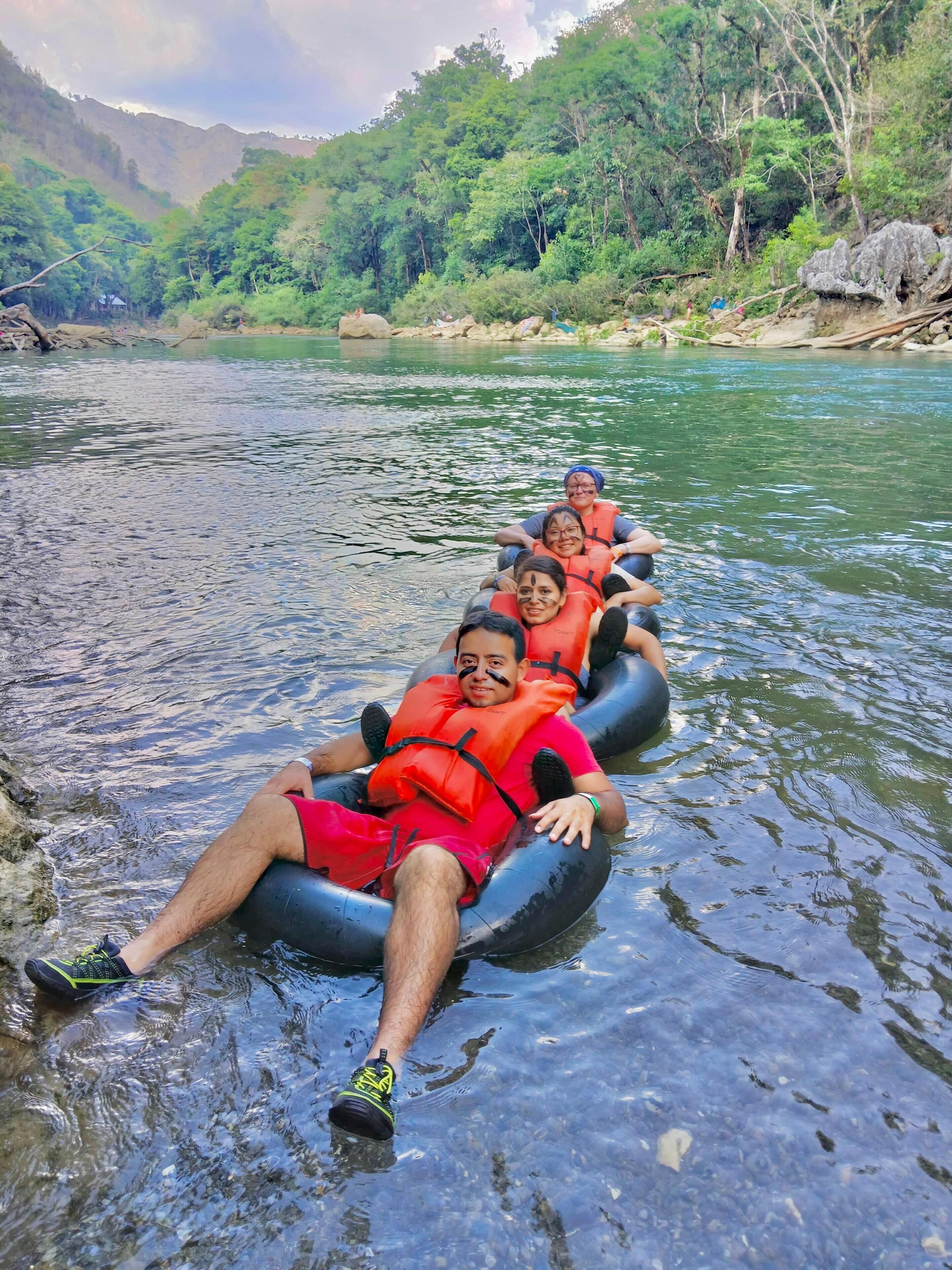 Personas haciendo rafting en un río, con chalecos salvavidas, rodeadas de un paisaje natural con árboles y colinas.