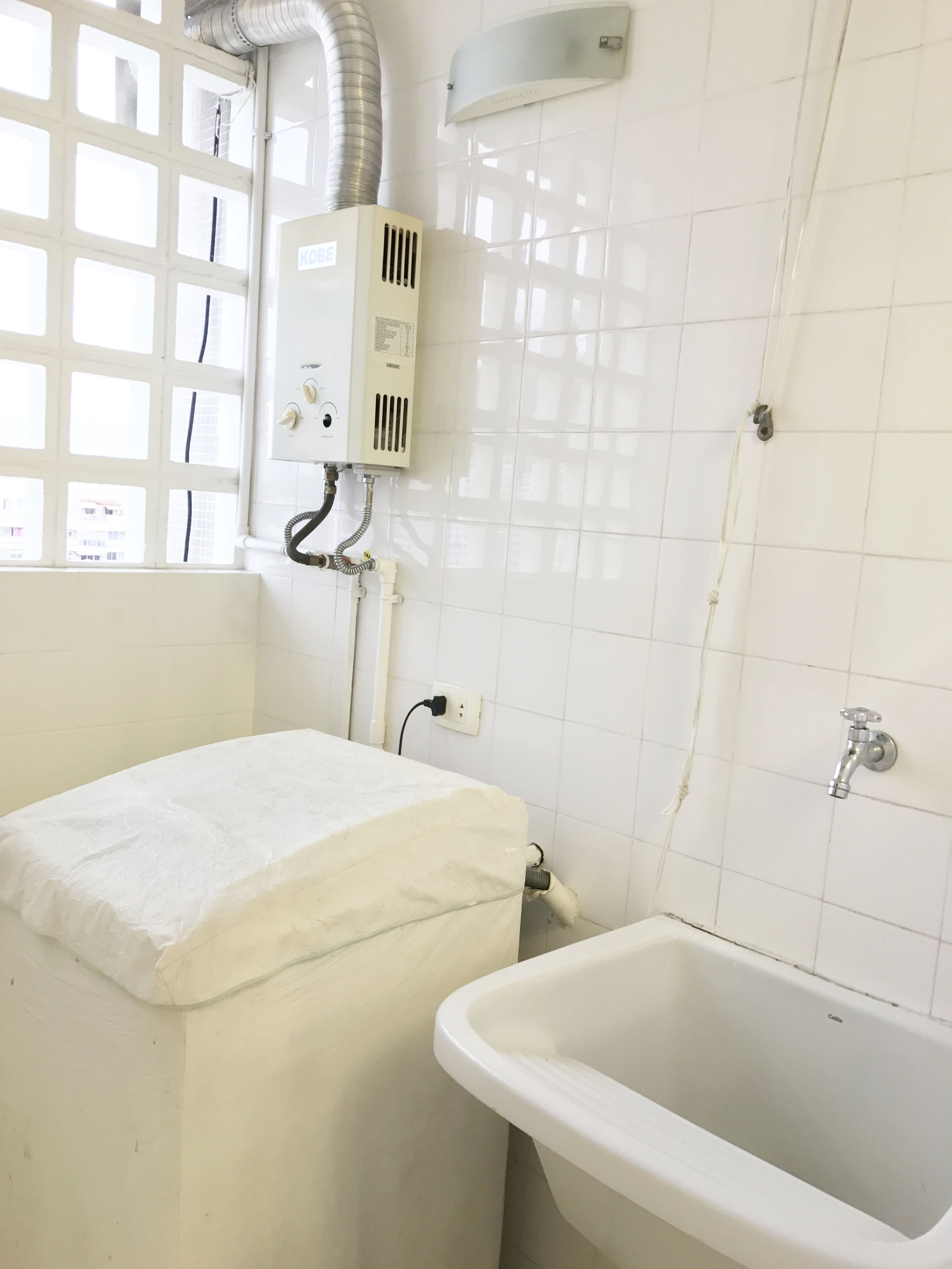 Une salle de bain avec une baignoire, une fenêtre donnant sur des immeubles et un chauffe-eau fixé au mur.