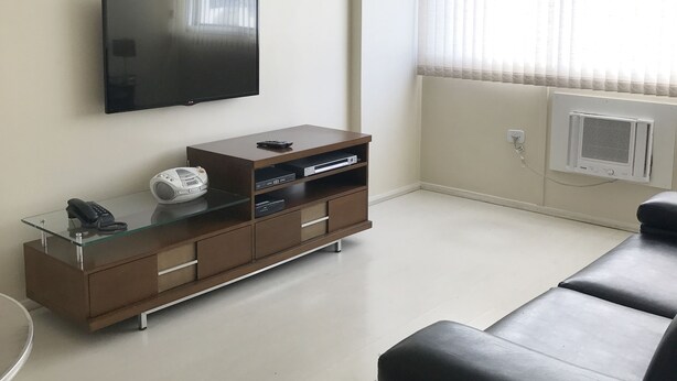 Una sala de estar moderna con un televisor de pantalla plana, una mesa de centro de vidrio, un mueble de entretenimiento marrón y un sofá negro.