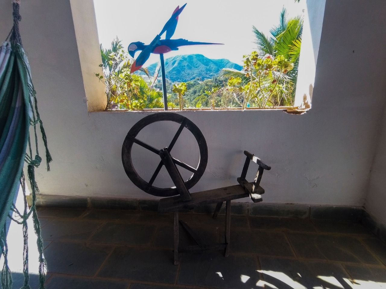 Un hamac, un rouet et une fenêtre donnant sur une montagne et des palmiers.