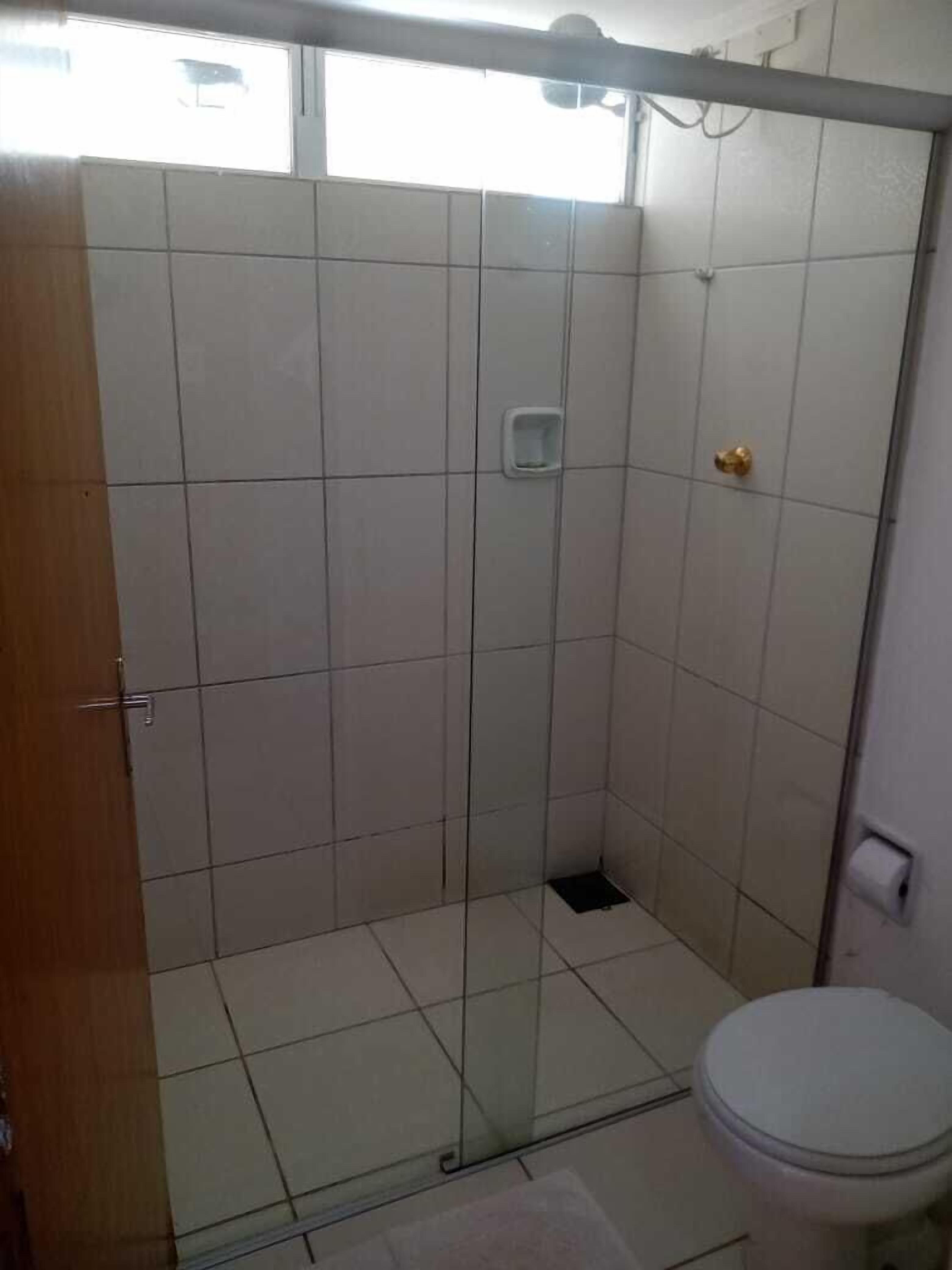 Un baño con cabina de ducha de vidrio, inodoro y una pequeña ventana.