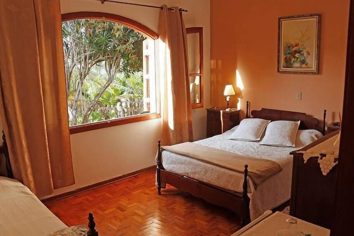 Ein Schlafzimmer mit einem hölzernen Bett, einem Nachttisch, einer Lampe, einem Fenster mit Vorhängen und einem Bild an der Wand.