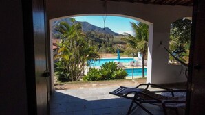 An open doorway leading to a patio with a pool, lounge chairs, and a view of a mountainous landscape. - Pousada Amanhecer na Mantiqueira (Águas de Lindóia)