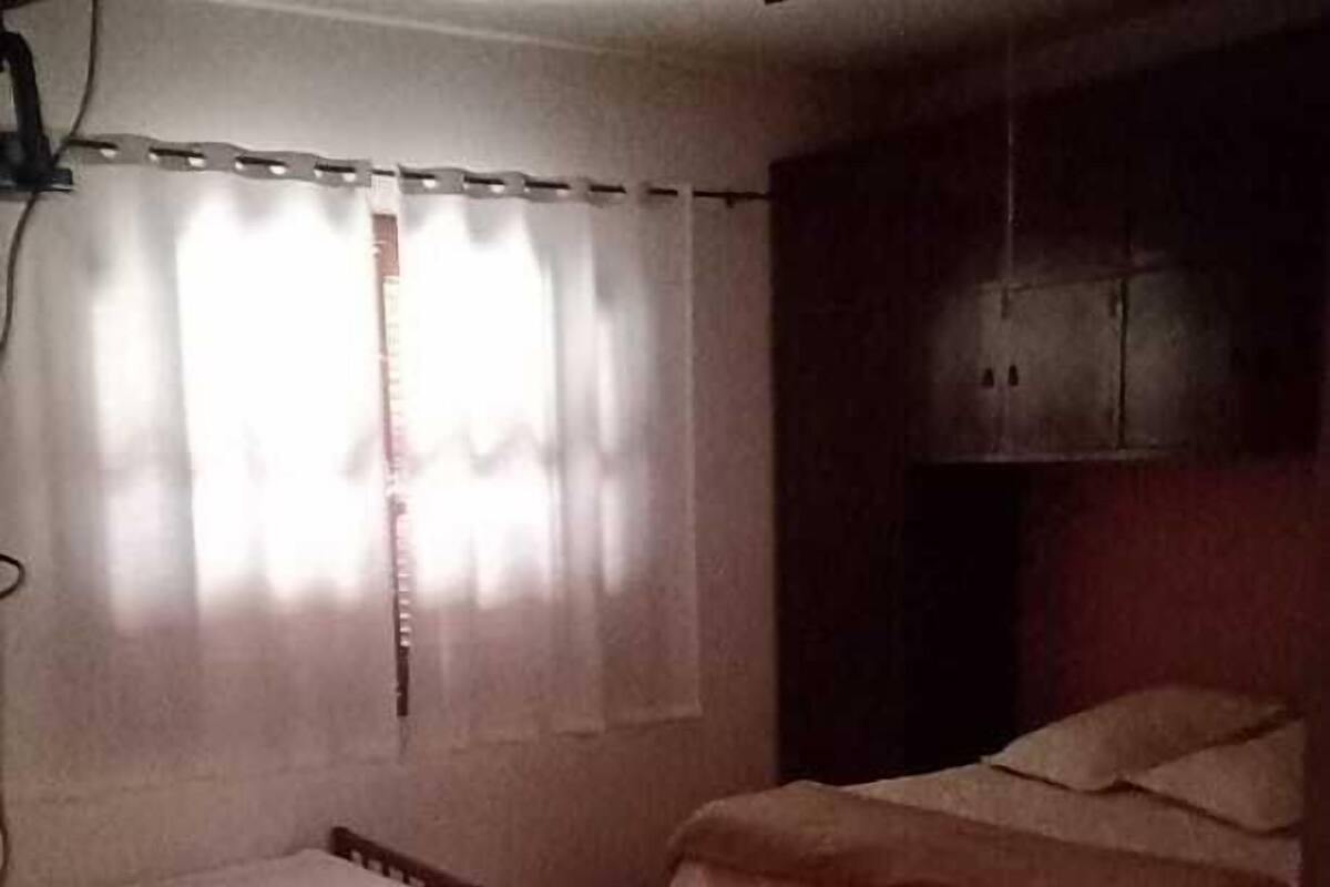 Ein Zimmer mit einem Bett, einem kleinen Tisch und einem Fenster mit Vorhängen.
