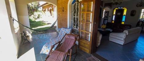 A covered outdoor seating area with a hammock, a table with a patterned tablecloth, and a lounge chair.