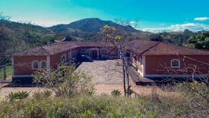 A two-story building with a red-tiled roof, a central courtyard, and a mountainous backdrop. - Pousada Amanhecer na Mantiqueira (Águas de Lindóia)