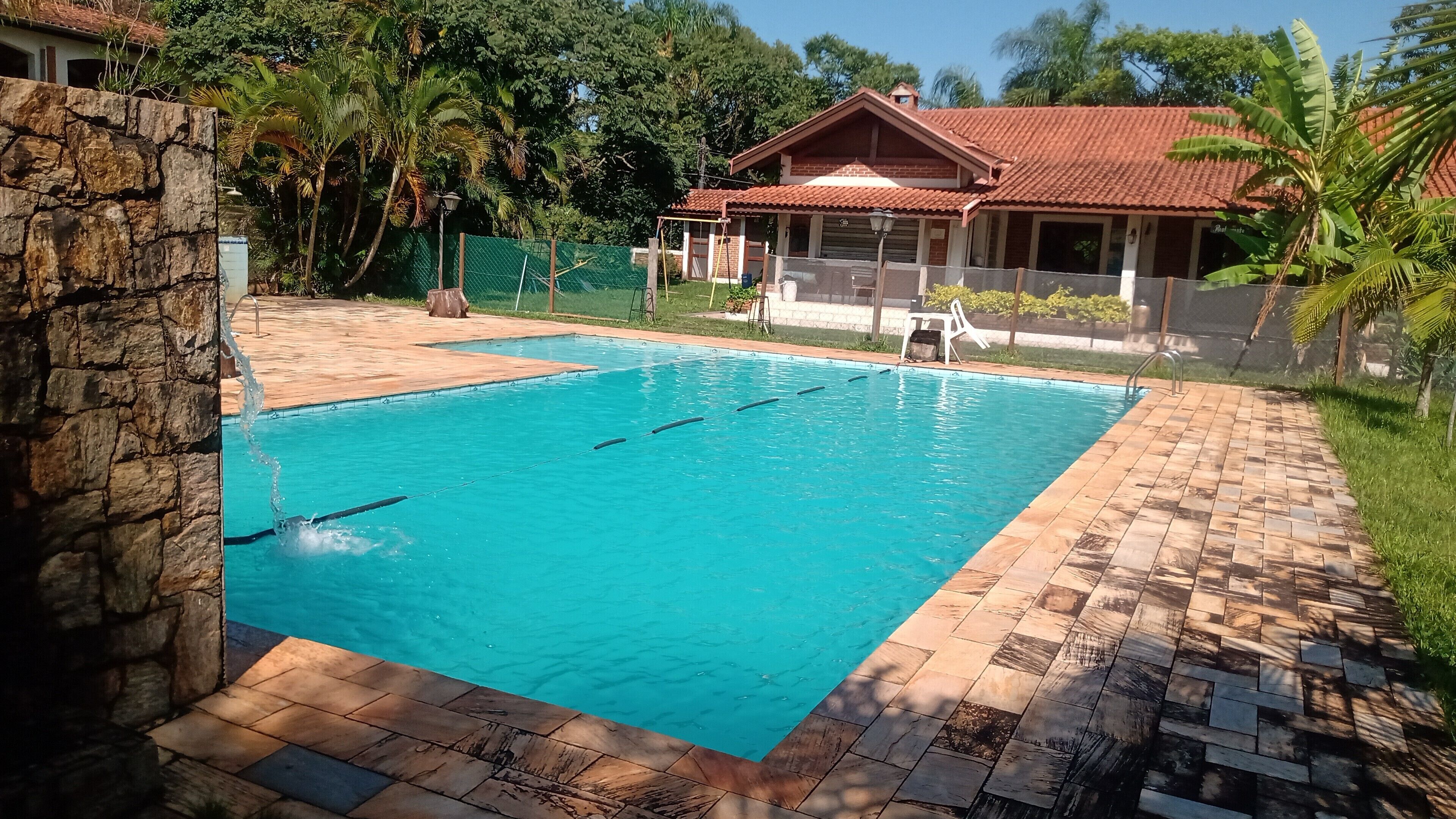 Una piscina con un muro de piedra a un lado y una zona de solárium con baldosas.