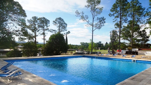 Una piscina rectangular con borde de baldosas, rodeada de árboles y un cielo despejado.