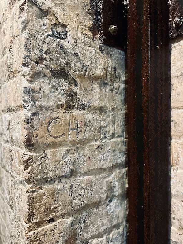 Un gros plan d’un mur de pierre érodé par les intempéries, sur lequel on peut voir l’inscription « CH ».