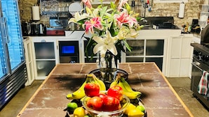 Uma cozinha com bancada de mármore, um vaso de flores e uma fruteira.