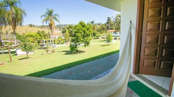 A view from a balcony with a hammock, a green lawn, palm trees, and a wooden door.