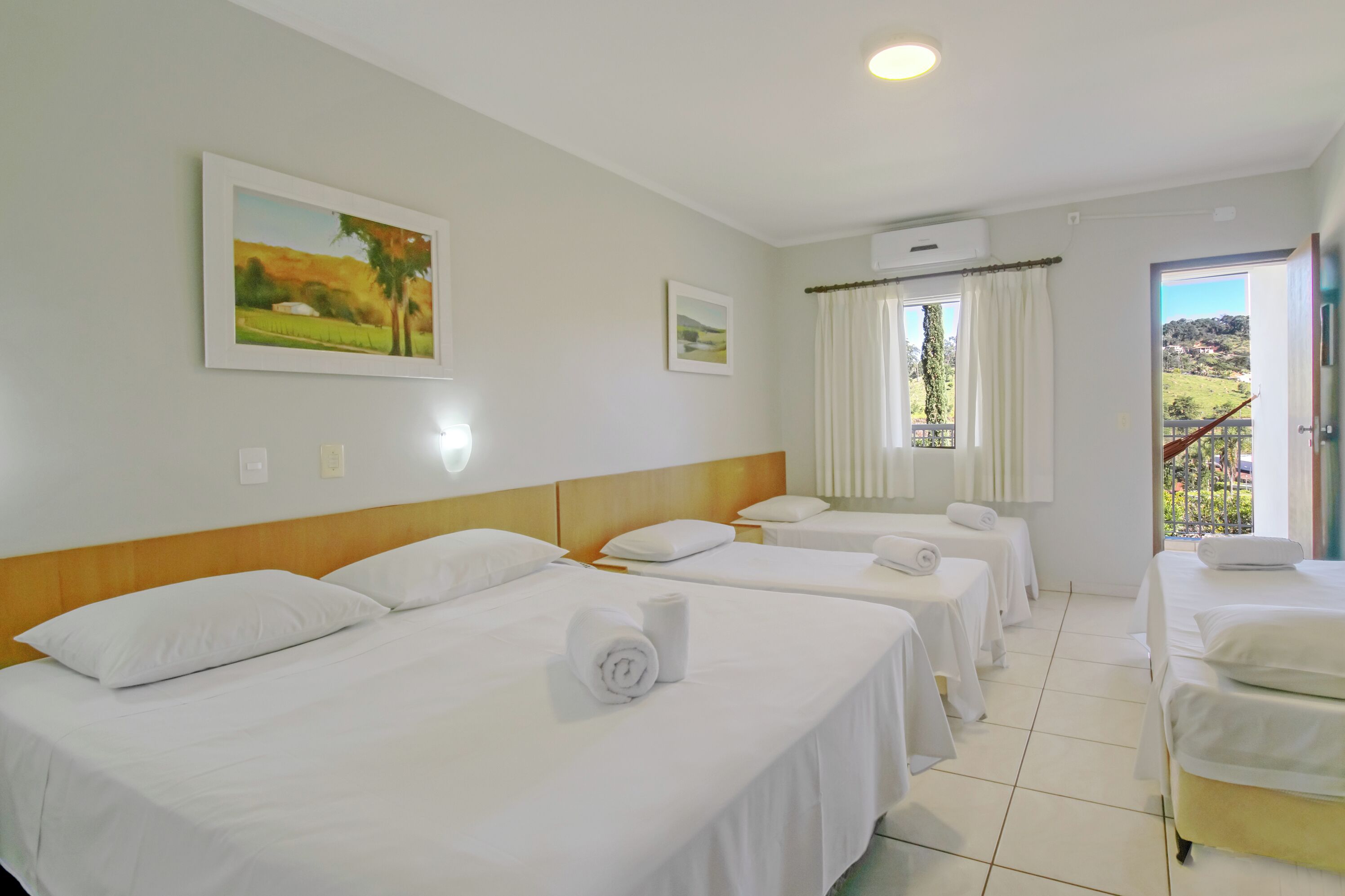 A hotel room with three beds, a large window with curtains, and a painting on the wall.