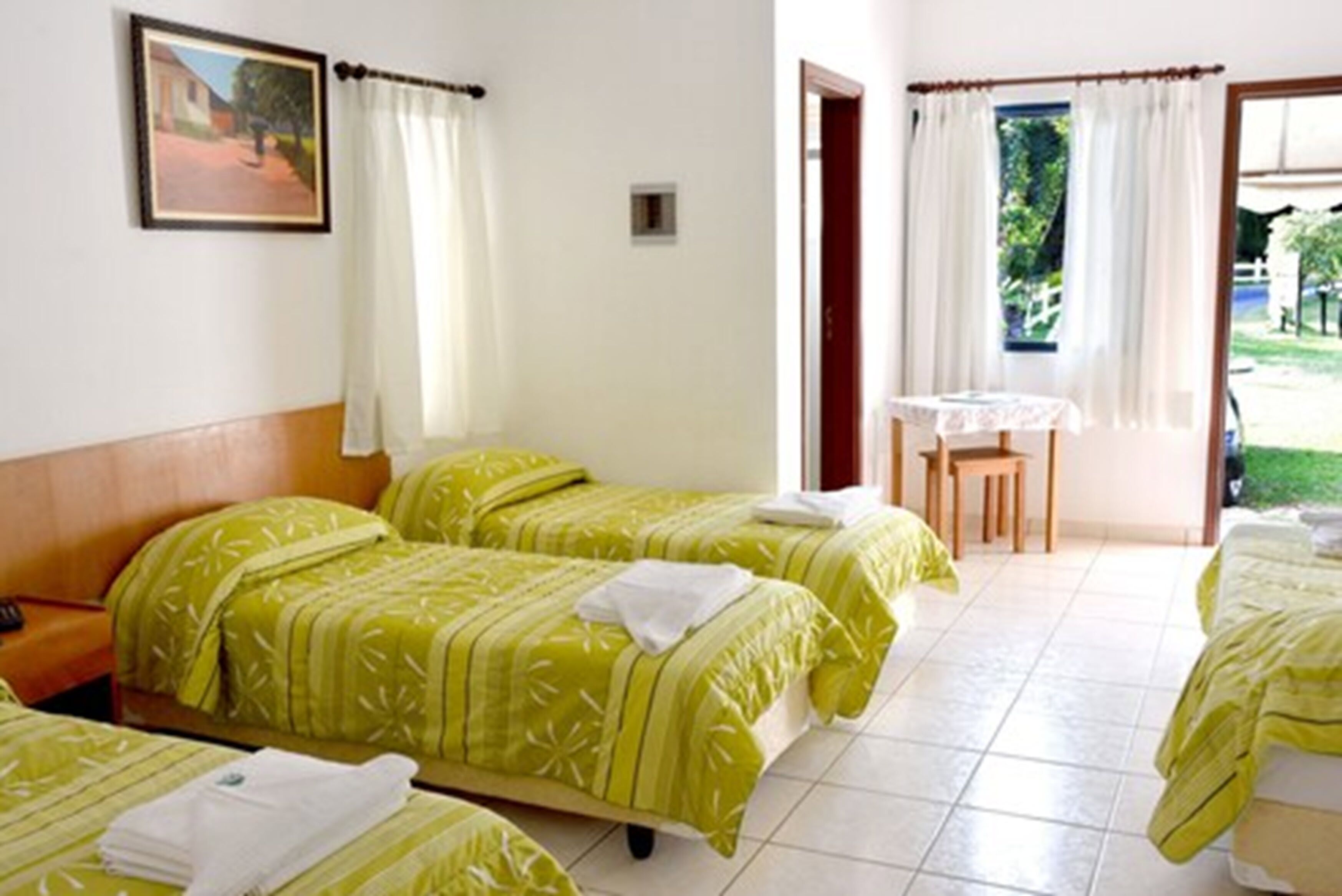 Quarto de hotel com duas camas, uma mesinha e vista para o jardim.