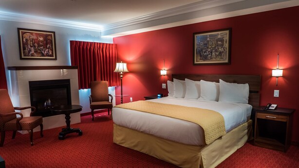 Une chambre d’hôtel avec un grand lit, une cheminée, un bureau avec une chaise et deux lampes fixées au mur.