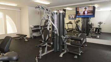 A gym with various exercise machines, a television screen, and a mirror.
