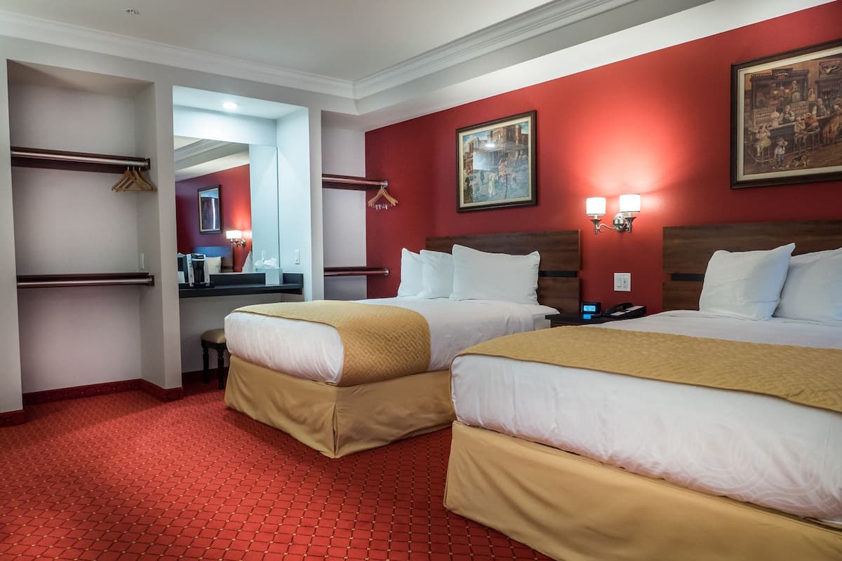 Hotelkamer met twee bedden, rode wanden, een roodgekleurd tapijt, een bureau met een computer en een spiegel.