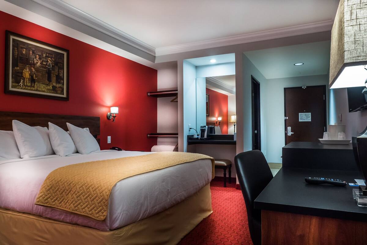 Een hotelkamer met een groot bed, een bureau met stoel, een kleine tafel met lamp en een schilderij aan de muur.